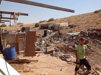 A Palestinian boy standing in front of demolished structures in Abu Kbash, 4 August 2021. Photo by OCHA
