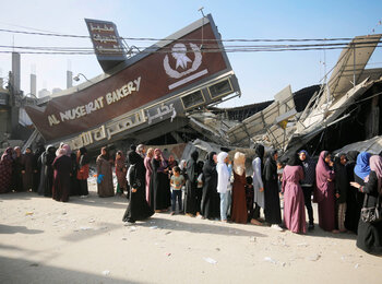 نساء وفتيات يقفن في طوابير أمام مخبز مدمر للحصول على الخبز في قطاع غزة.  قُصف 11 مخبزًا ودُمر منذ 7 تشرين الأول/أكتوبر. وفي جنوب غزة، لا تملك المطحنة الوحيدة العاملة القدرة على طحن القمح بسبب انقطاع الكهرباء والوقود. تصوير الأونروا