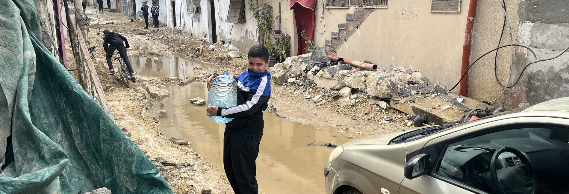 A Palestinian boy carrying water through a heavily damaged street of Tulkarm refugee camp, following an Israeli operation that involved drone strikes and road bulldozing. Photo by OCHA