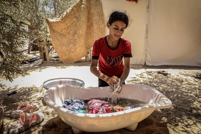 فتاة نازحة تغسل ثيابًا في مخيم للاجئين في خانيونس. تصوير منظمة الصحة العالمية