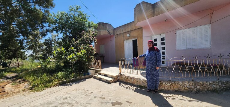 אום סאלח שרייתח עומדת בחזית ביתה באל־מזרעה אל־קיבלייה, מרכז הגדה המערבית. צילום: משרד האו״ם לתיאום עניינים הומניטריים.